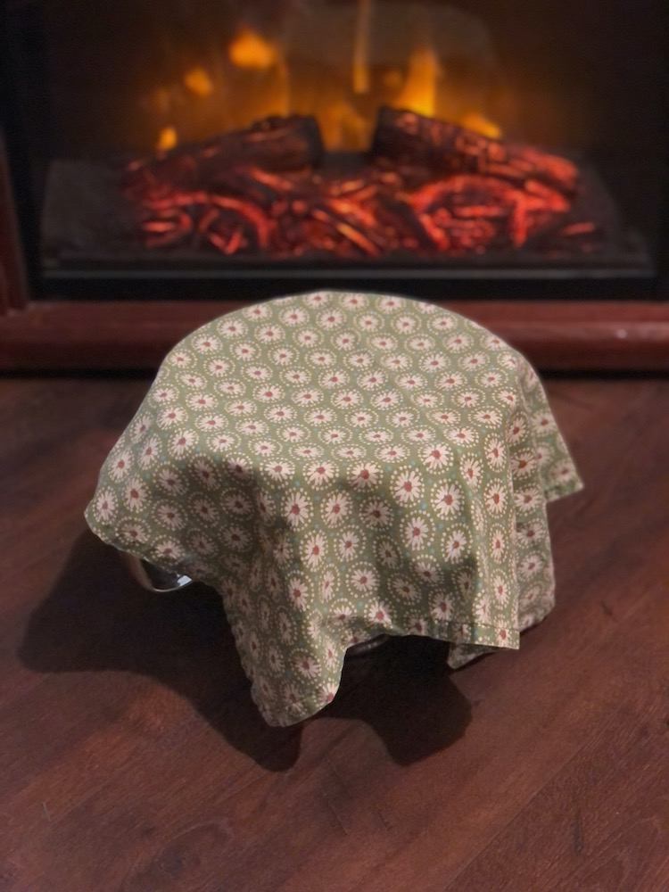 bread dough rising near a faux fireplace with a cloth napkin draped over it