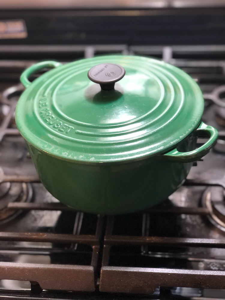 green le cruset dutch oven sitting on top of a cast iron stove