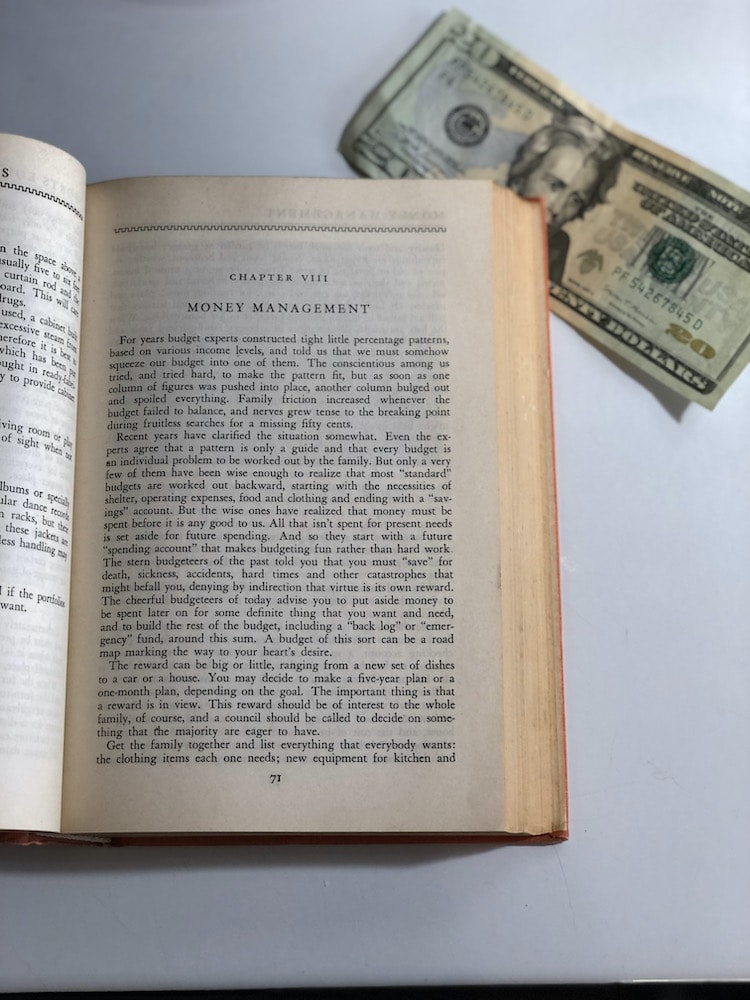 twenty dollar bill tucked under a old book, open to a chapter on money management