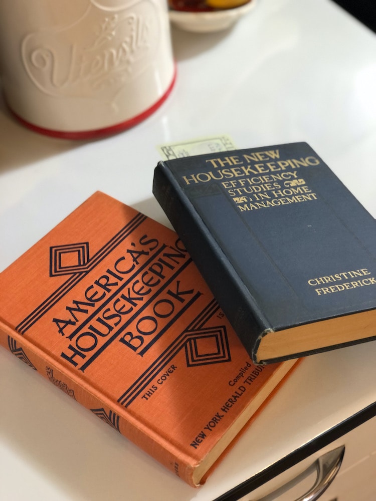 old homemaking books on a kitchen countertop with a twenty dollar bill used as a bookmark